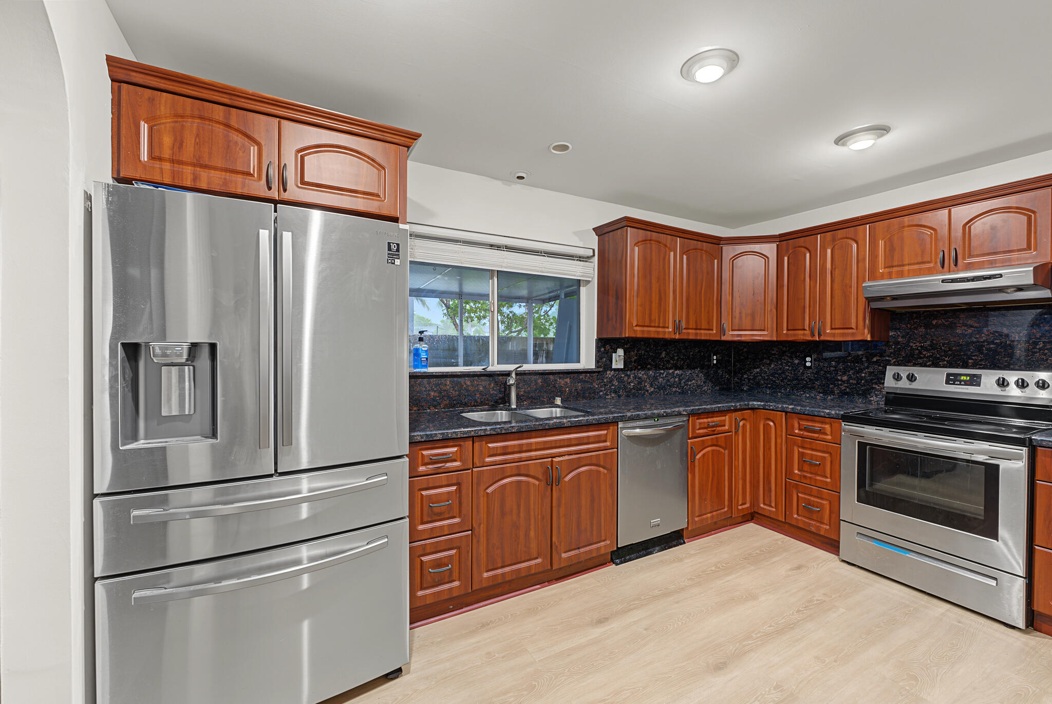 Kitchen featuring wood-finish cabinetry, stone-style countertops, stainless steel appliances, and wood-finish flooring