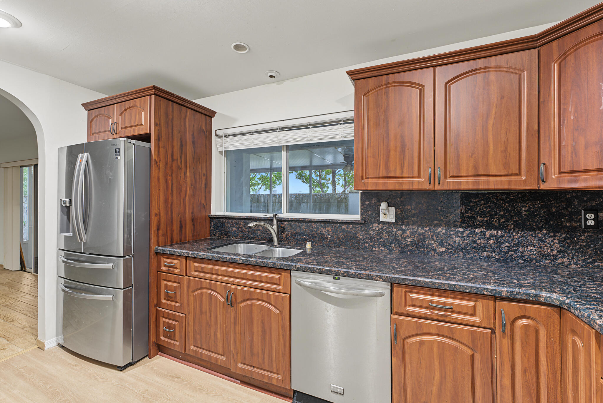Kitchen featuring stained wood cabinetry, stone countertops, stainless steel appliances, a double-basin sink, and arched doorway