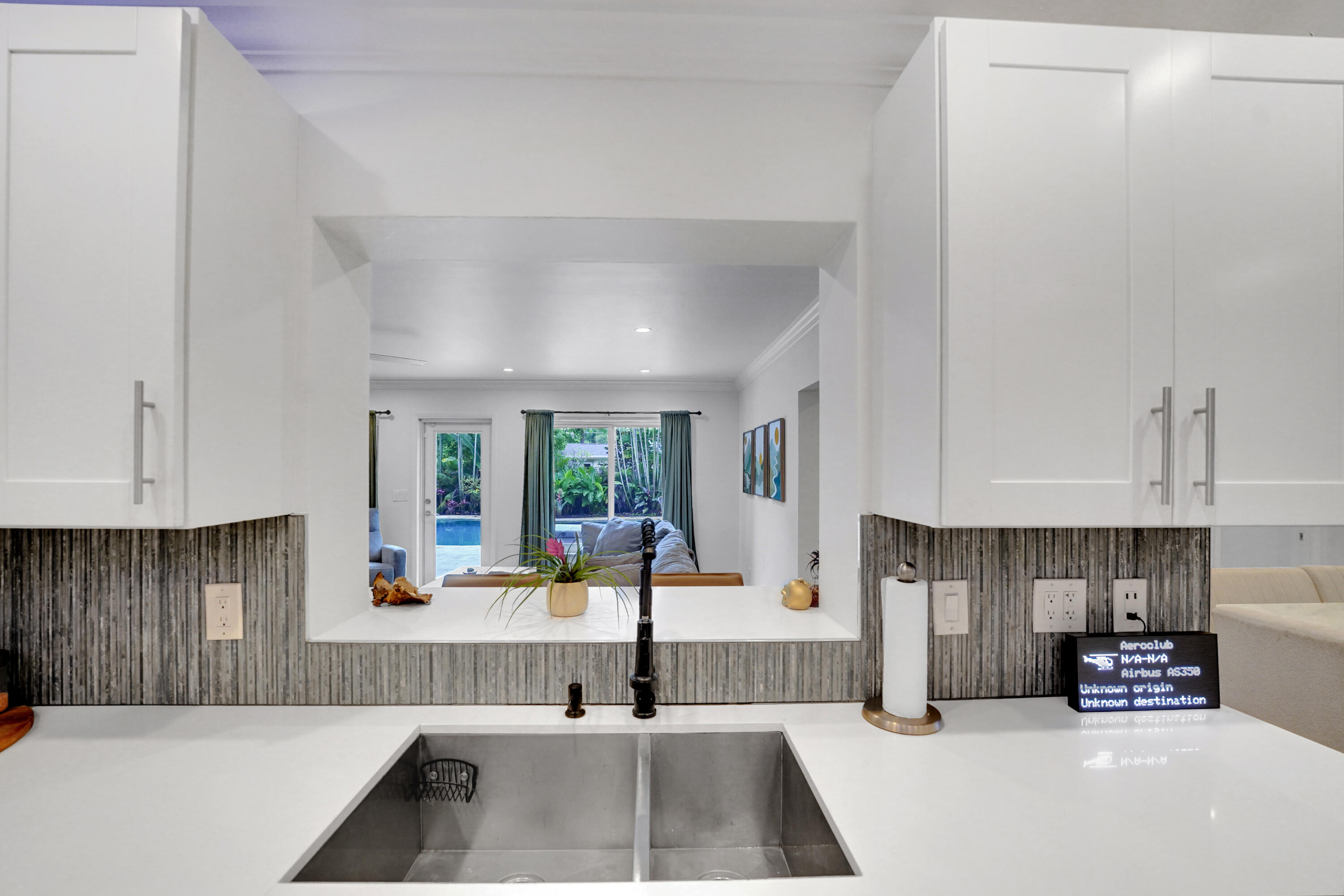 Kitchen featuring white shaker-style cabinetry, solid-surface countertops, a dual-basin stainless steel sink, matte black gooseneck faucet, and textured tile backsplash
