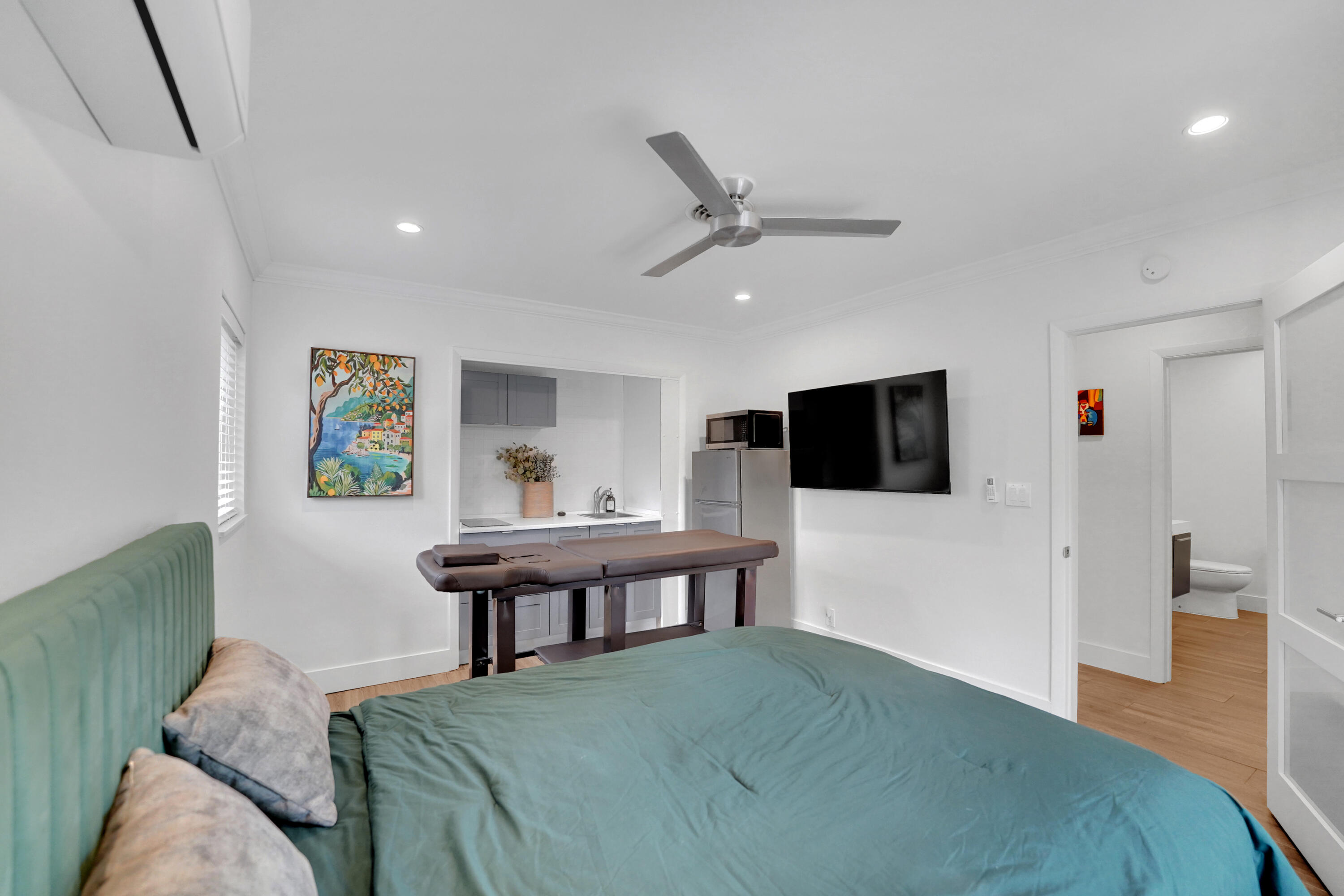 Interior space featuring recessed lighting, a ceiling fan, wood-finish flooring, a wall-mounted climate control unit, and a built-in kitchenette area with cabinetry and a sink
