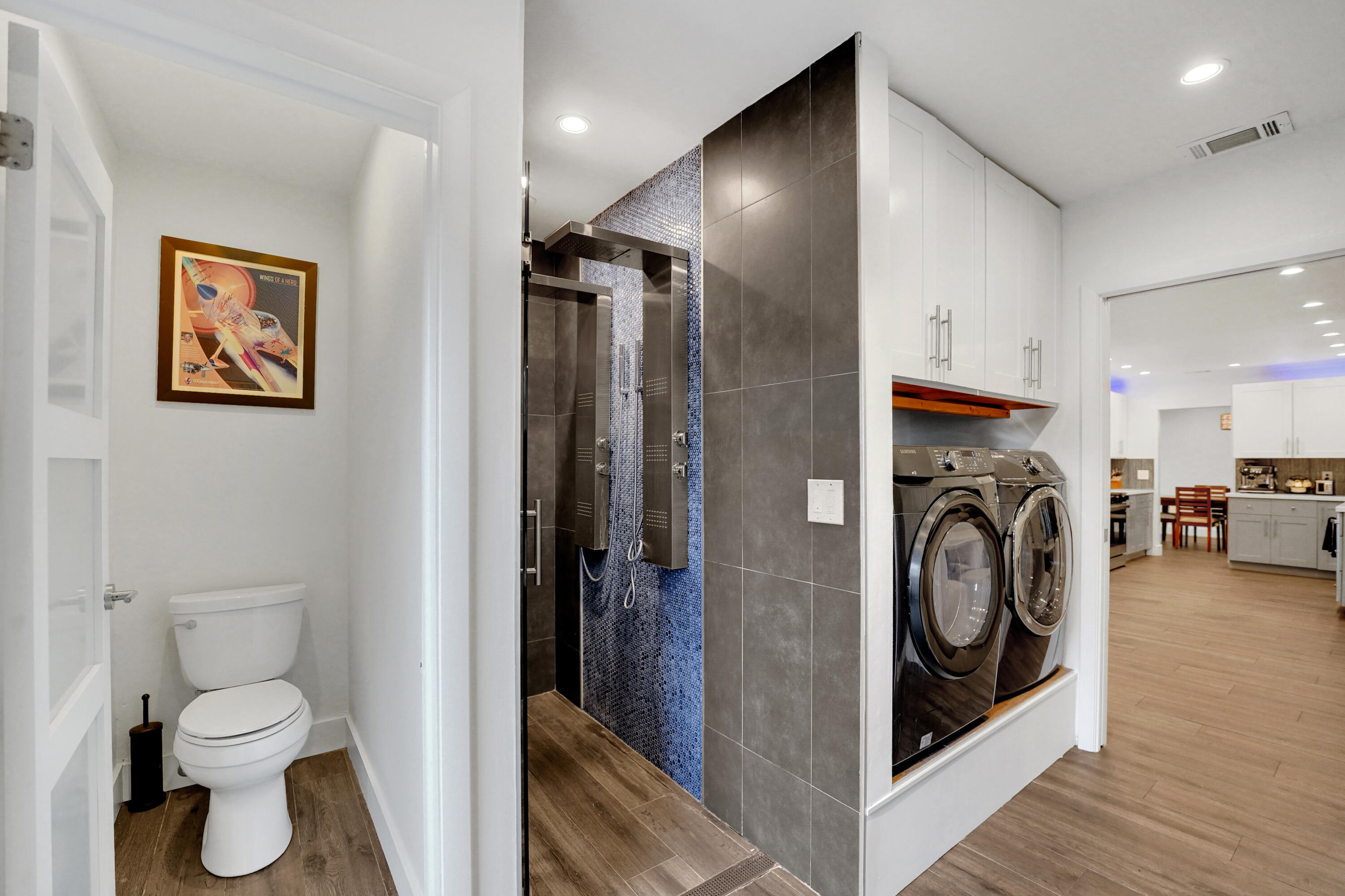 Shower stall with stainless steel multi-head panel and blue mosaic tile surround, built-in overhead cabinetry, and recessed lighting