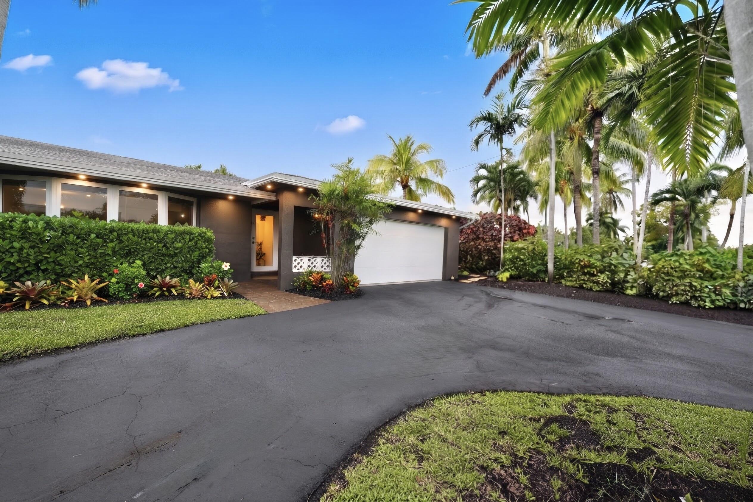 Exterior facade featuring a covered entryway, attached garage, stone-finish walkway, and mature landscaping with palm trees
