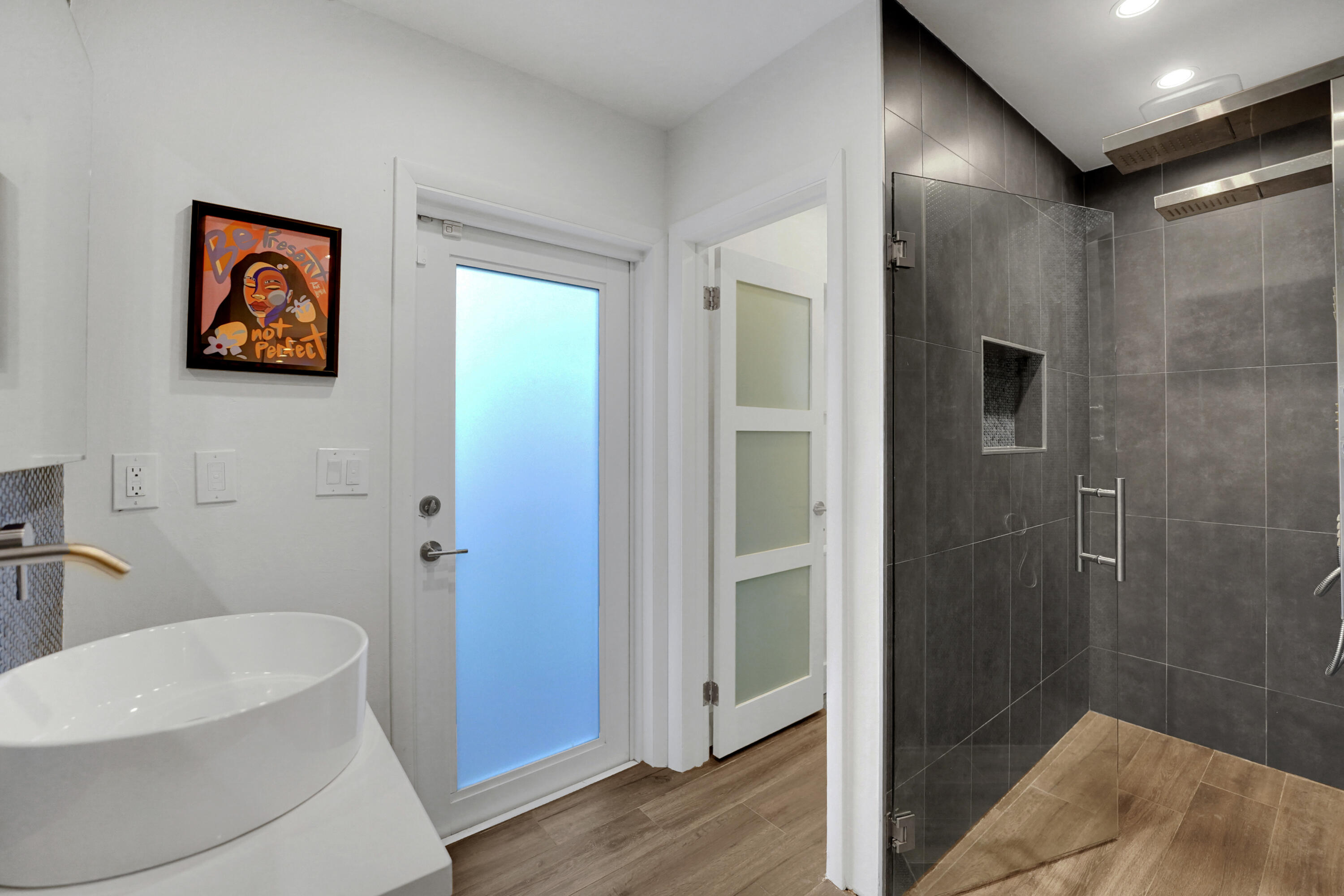 Bathroom featuring a vessel sink with a wall-mounted faucet, a glass-enclosed walk-in shower with dark tile surround and integrated niche, and frosted-glass panel doors
