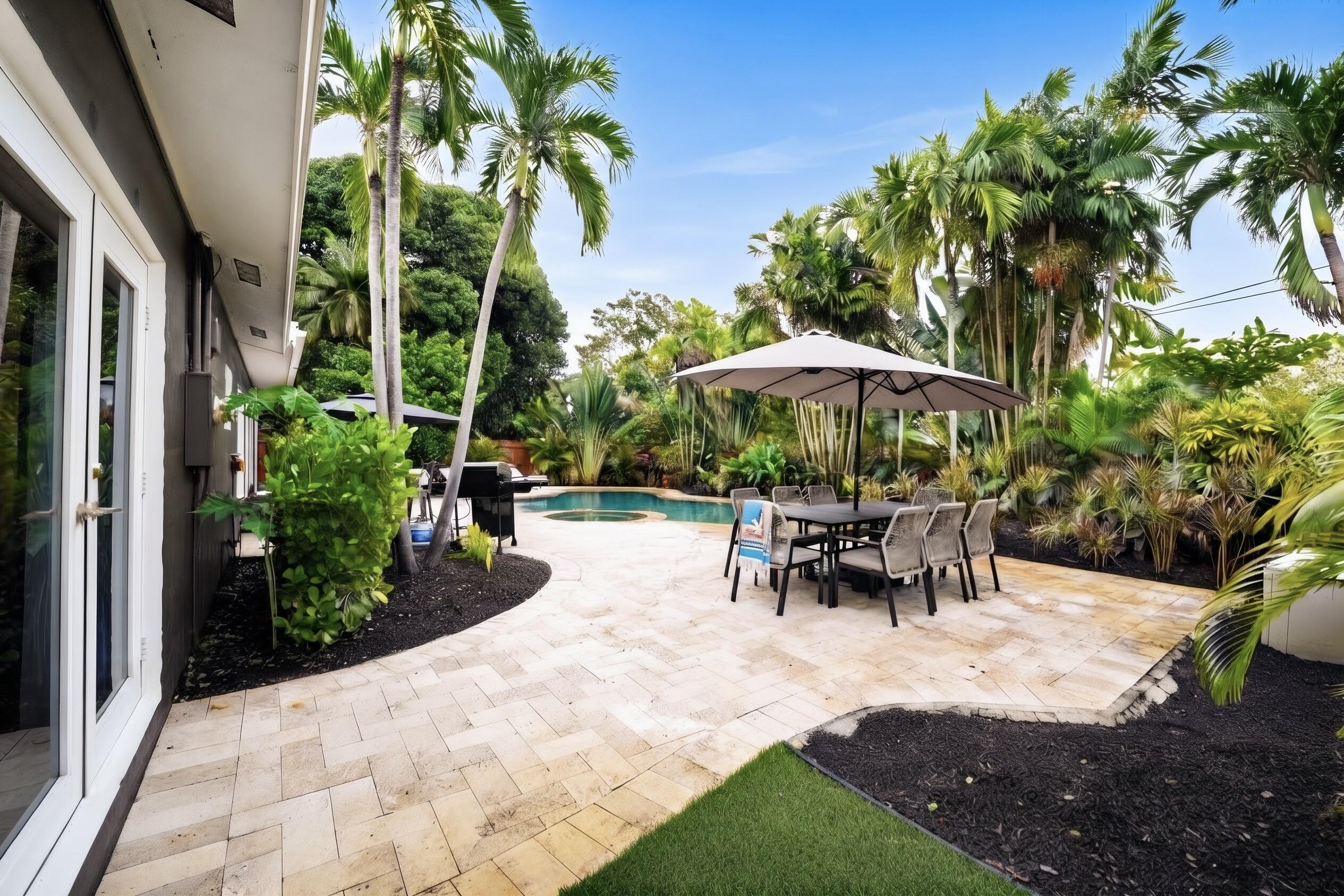 Backyard oasis featuring a paver patio, in-ground swimming pool with an attached spa, lush tropical landscaping, and mature palm trees