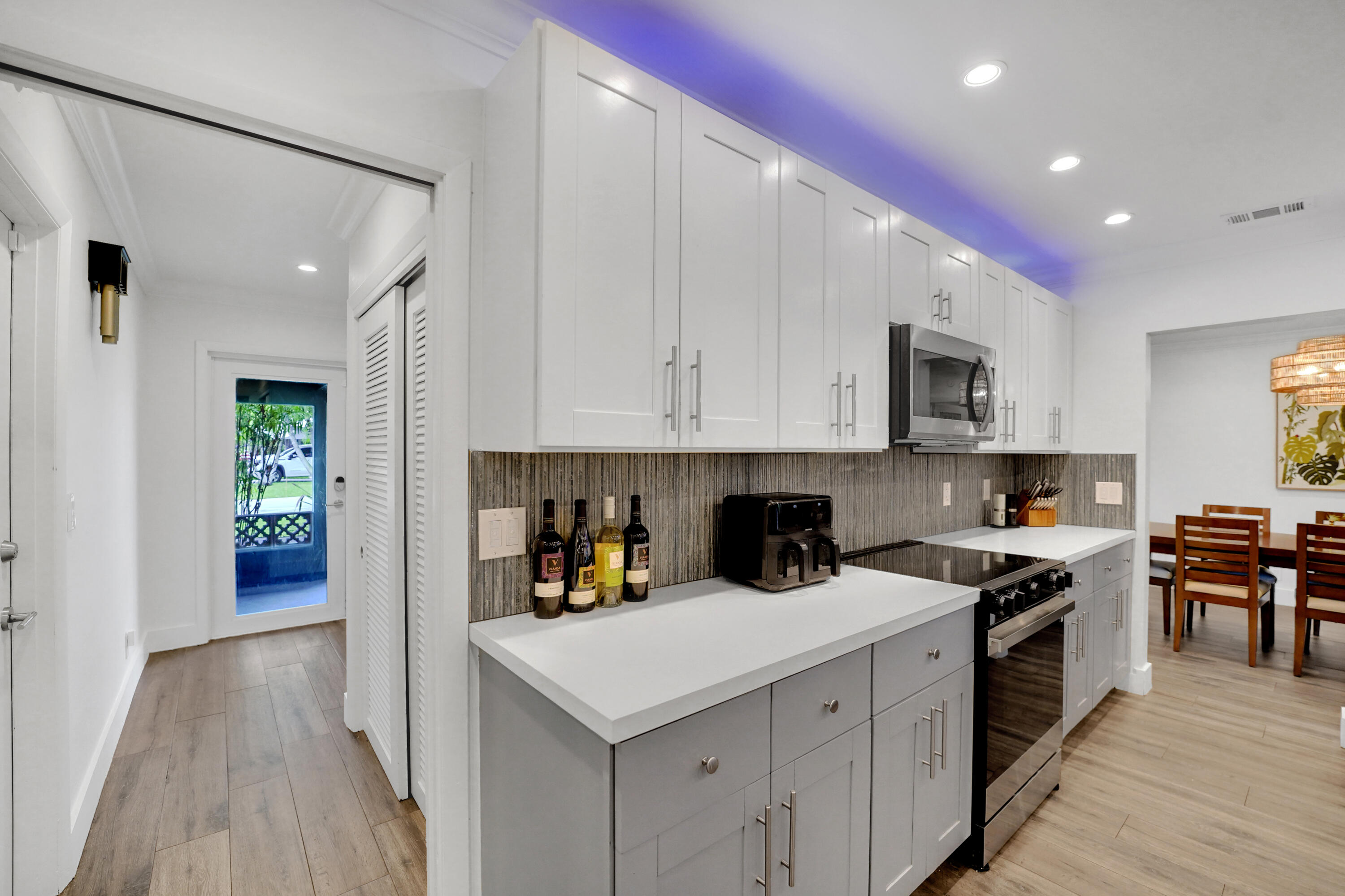 Kitchen featuring white upper cabinetry, grey base cabinetry, solid-surface countertops, textured tile backsplash, and recessed lighting