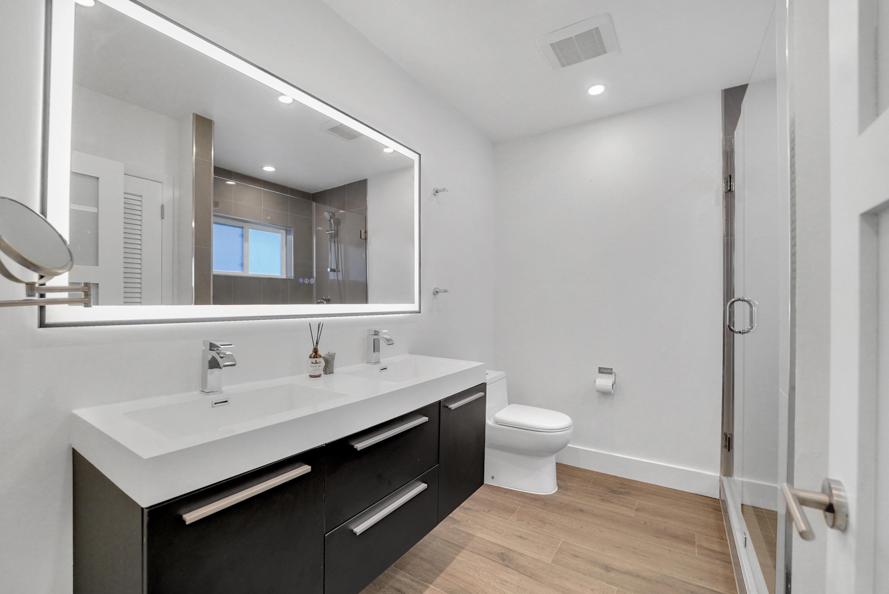 Bathroom featuring a dual-sink vanity with dark cabinetry and a stone countertop, a large integrated LED-lit mirror.