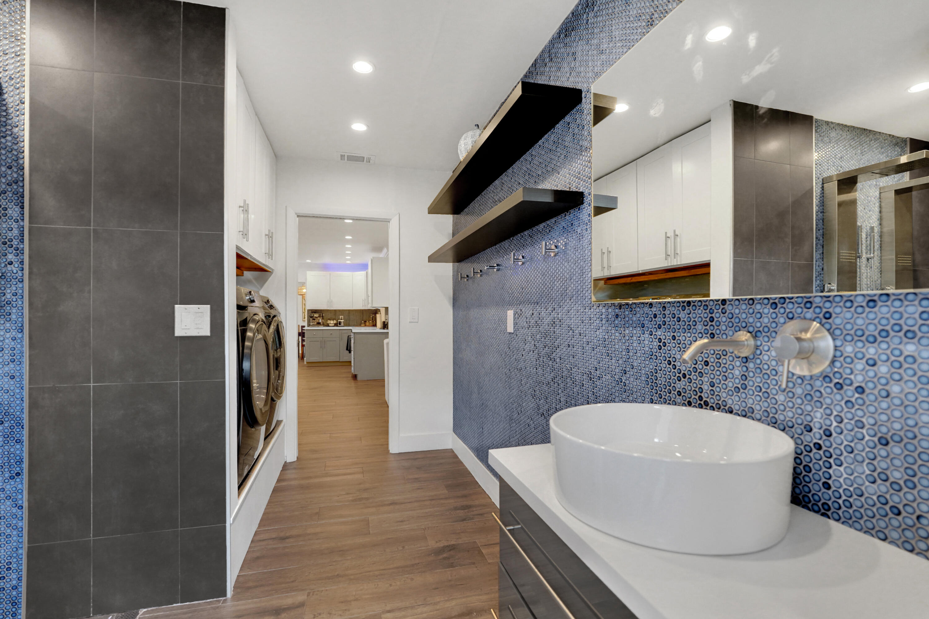 Vessel sink with a wall-mounted faucet, custom vanity with a quartz countertop, blue circular mosaic tile backsplash, built-in floating shelves