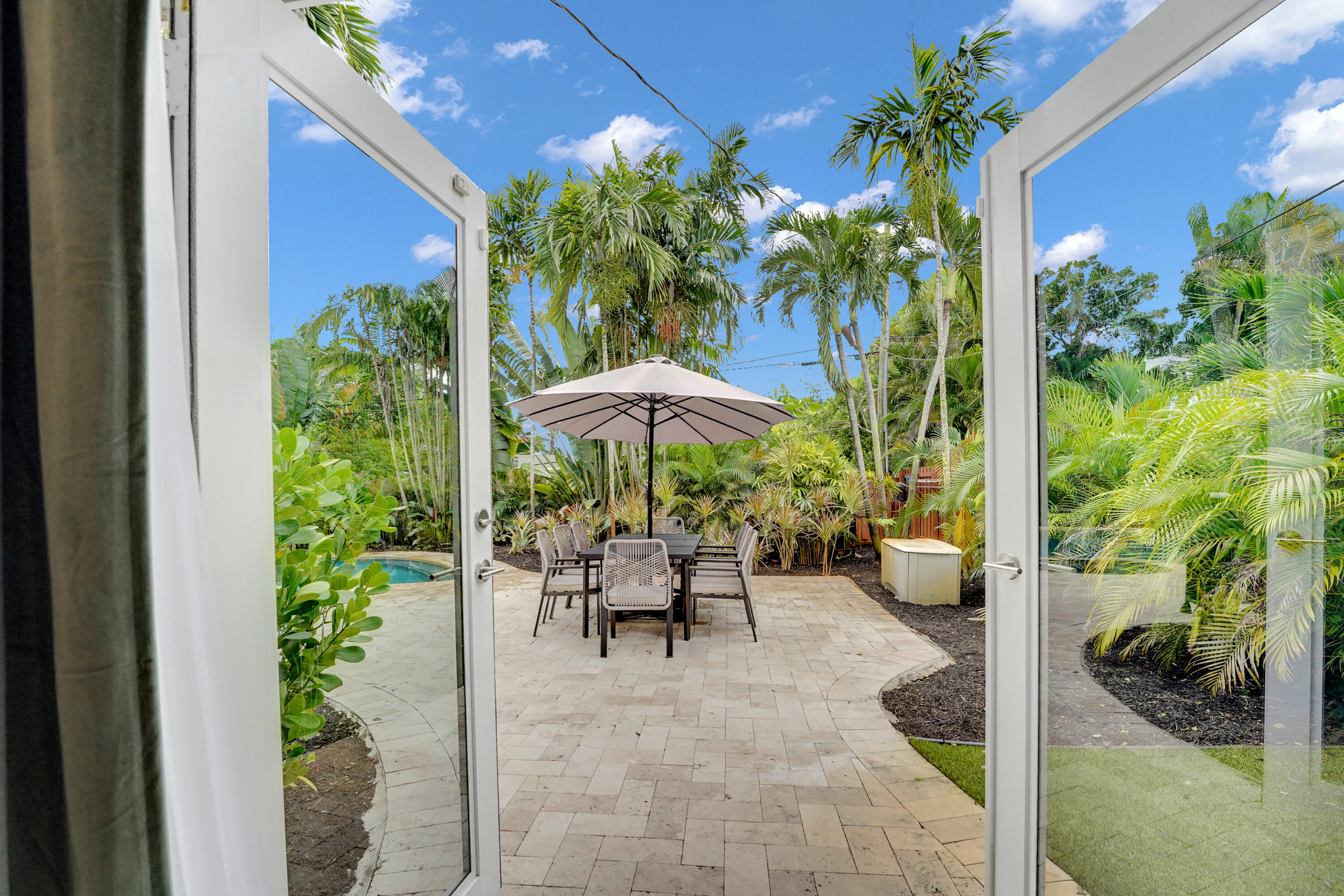 Paver patio featuring a built-in swimming pool, surrounding lush landscaping, and white-framed French door entry