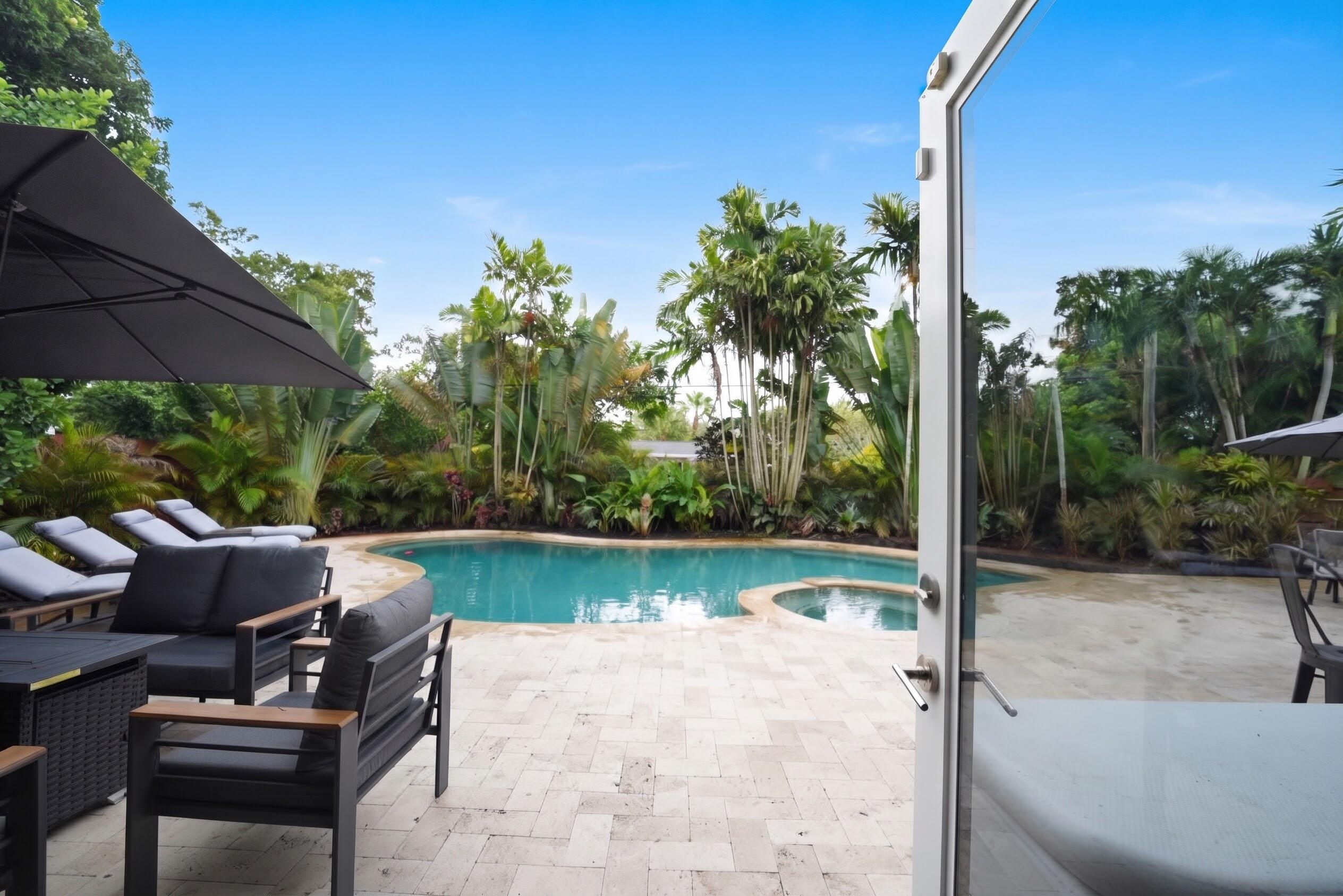 Backyard area featuring a swimming pool with integrated spa, paved stone decking, and mature tropical landscaping
