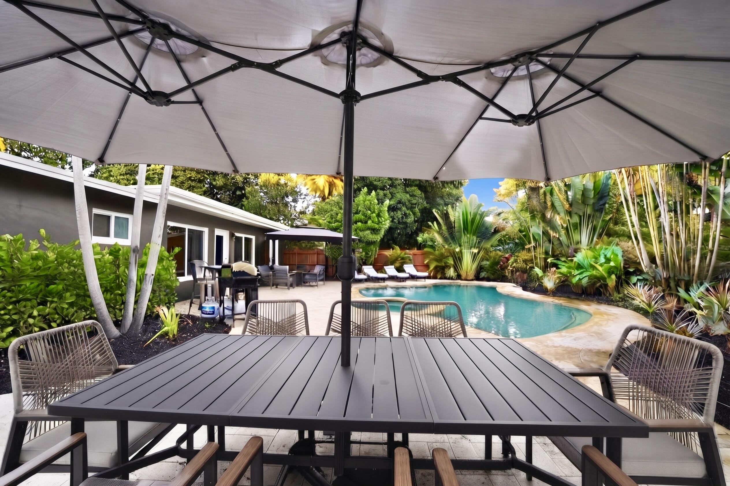 Outdoor patio featuring stone-paver hardscaping, a swimming pool with an attached spa, and mature tropical landscaping