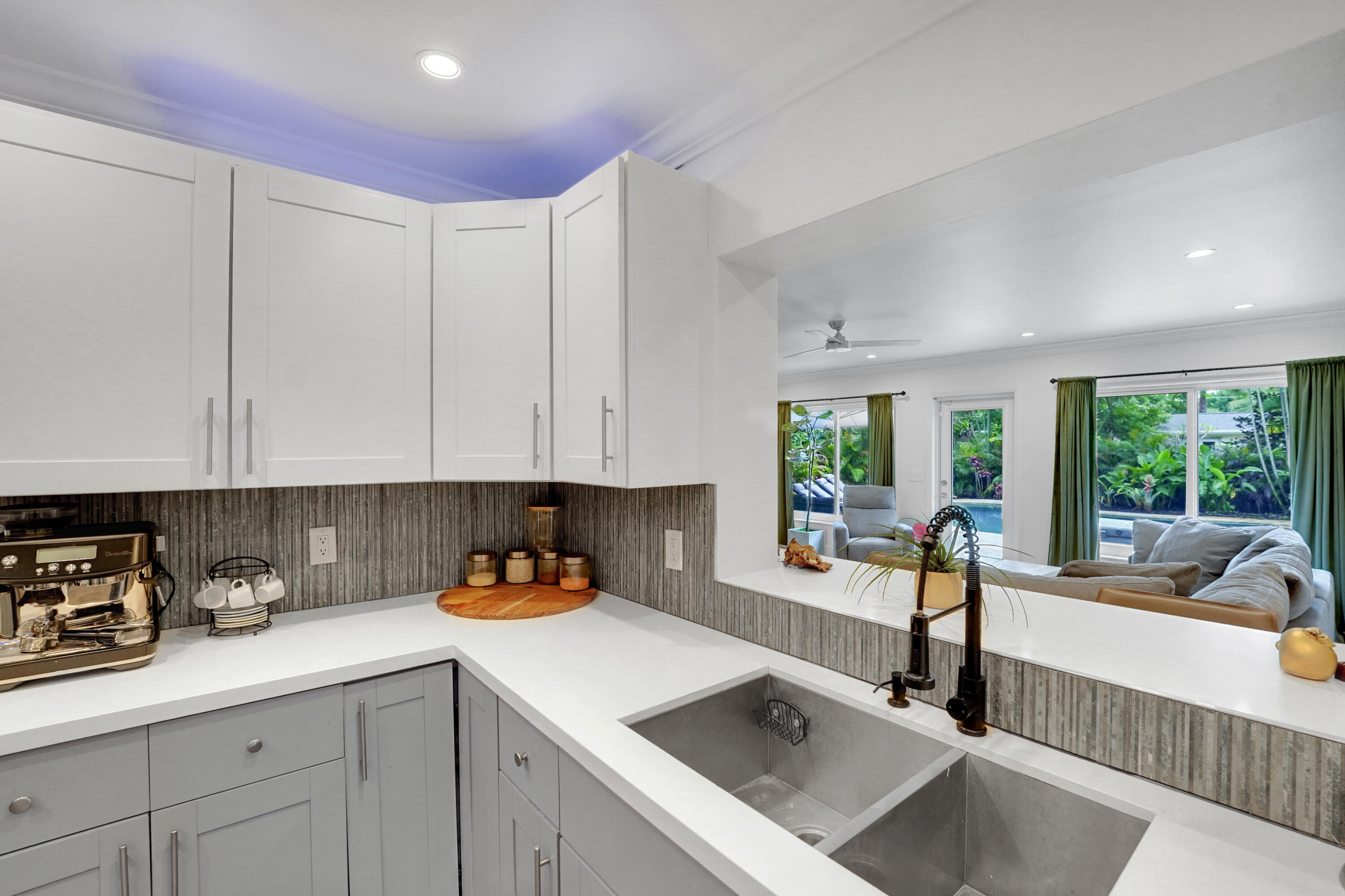 Kitchen featuring white upper cabinetry, grey lower cabinetry, white countertops, a textured tile backsplash, and a dual-basin stainless steel sink with a high-arch matte black faucet