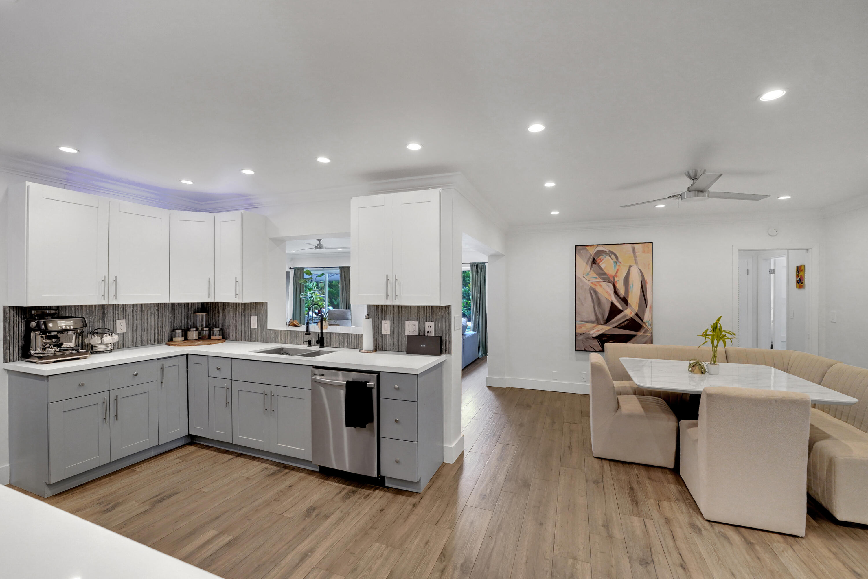 Kitchen featuring two-tone shaker-style cabinetry, quartz countertops, tile backsplash, stainless steel dishwasher.