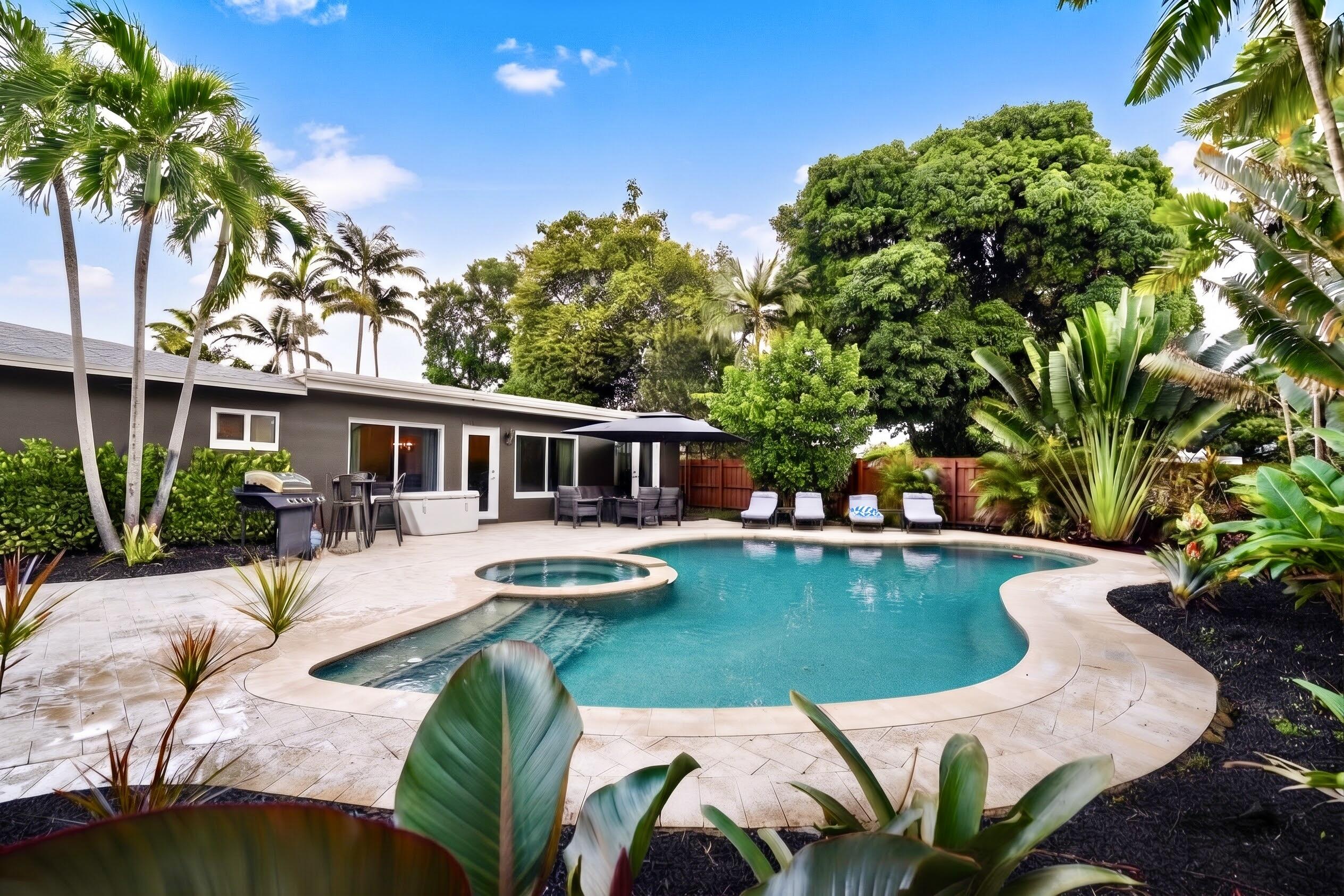 Backyard oasis featuring an in-ground pool with an integrated spa, stone-paver patio, mature palms, and tropical landscaping
