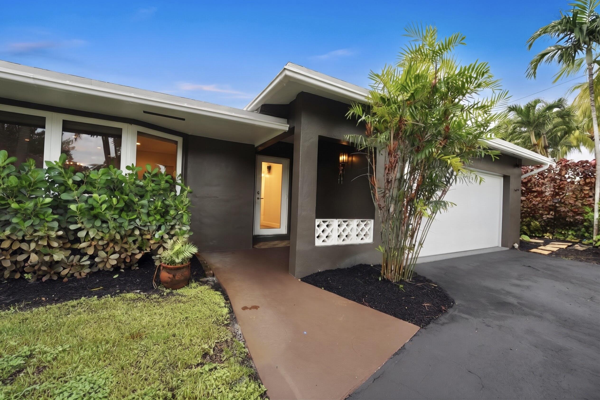 Stucco exterior facade featuring a covered entryway, decorative breeze block accents, oversized windows, and a paved driveway