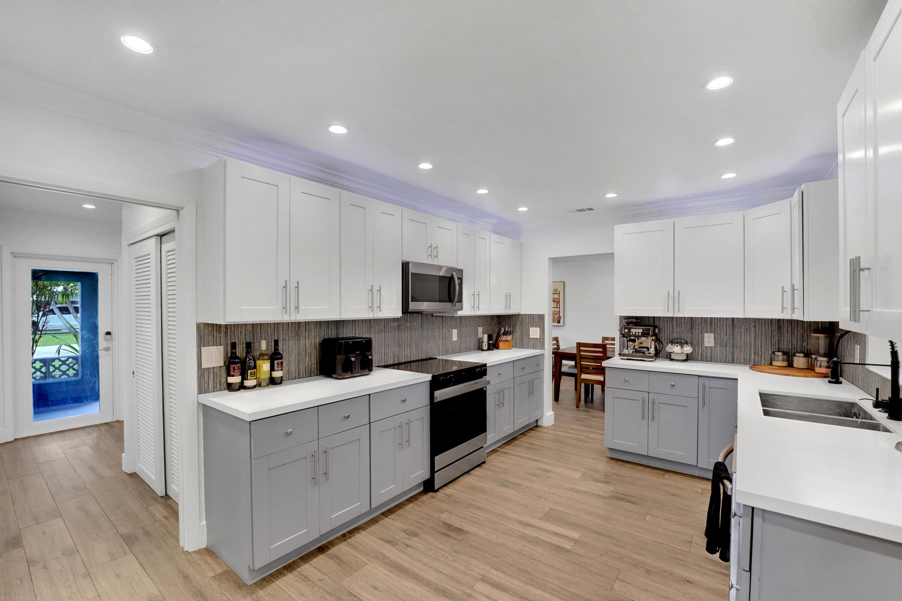 Kitchen featuring two-tone shaker-style cabinetry, quartz countertops, tile backsplash, recessed lighting, and wood-finish flooring