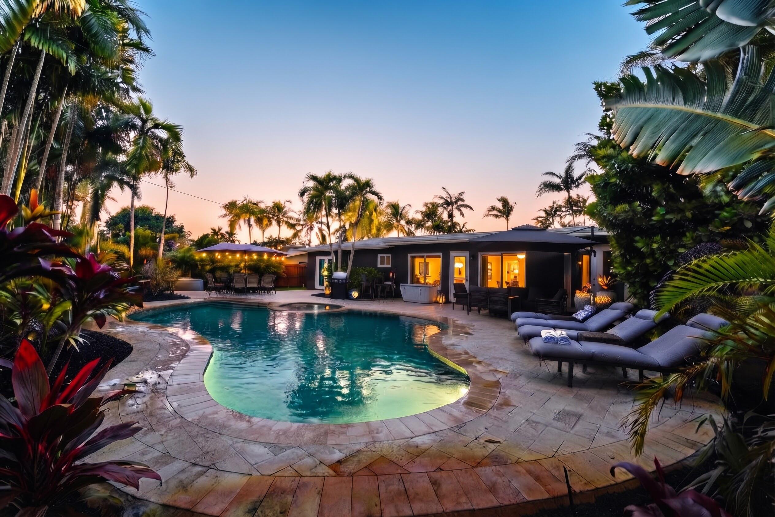 Freeform swimming pool with stone coping, expansive paver patio, integrated spa, and mature tropical landscaping