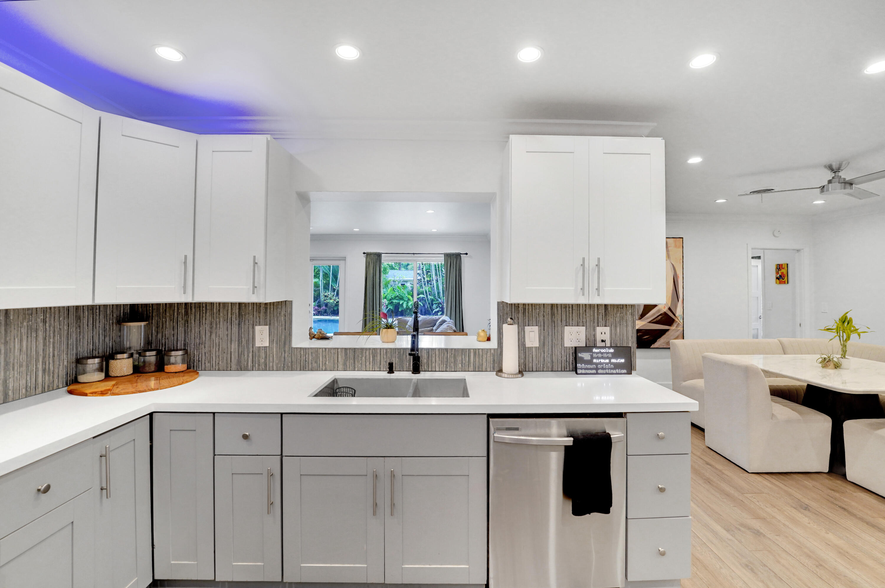 Kitchen featuring white upper cabinetry, grey lower cabinetry, white countertops, stainless steel dishwasher, and textured tile backsplash