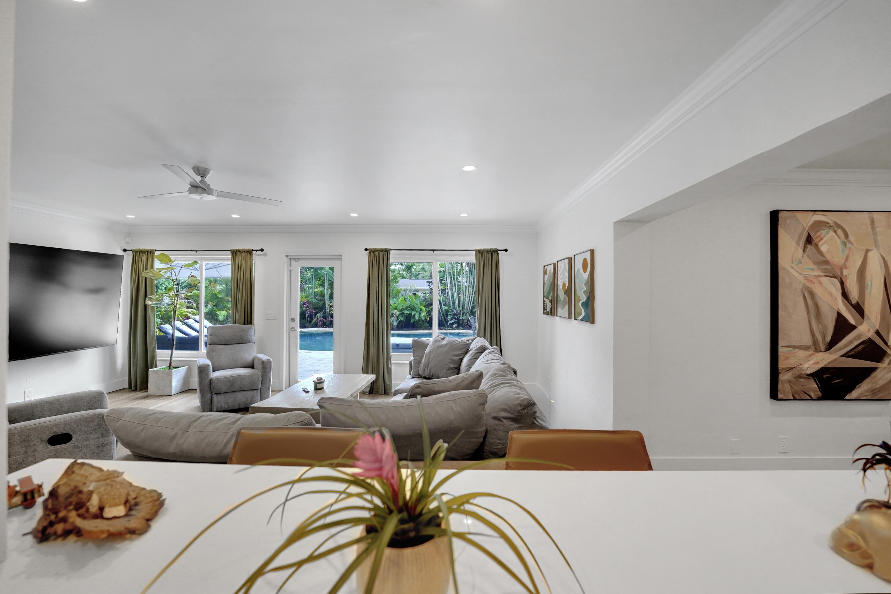 Open-concept interior featuring recessed lighting, crown molding, a white countertop peninsula, and multiple windows with exterior pool access