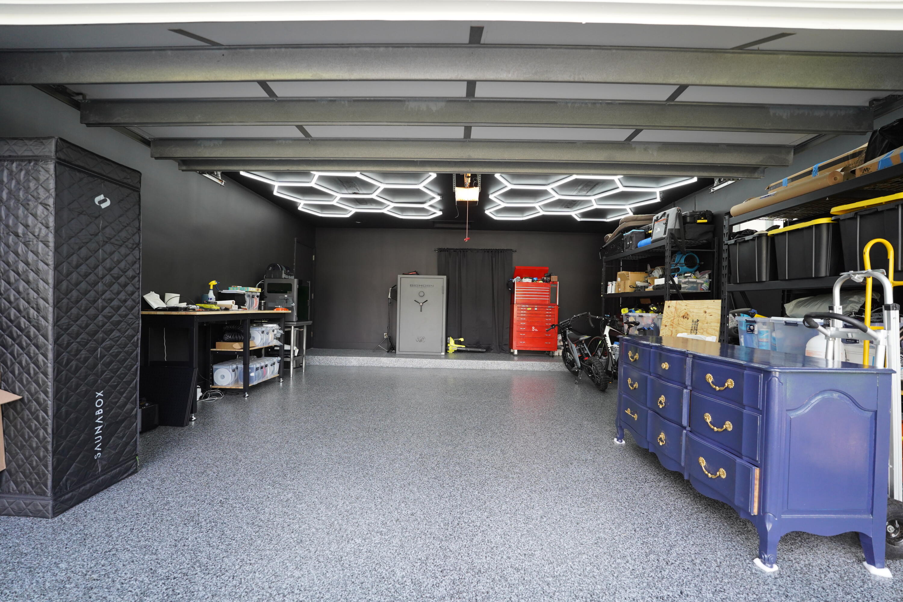 Garage featuring epoxy-coated flooring, matte black wall finishes, and geometric LED ceiling lighting