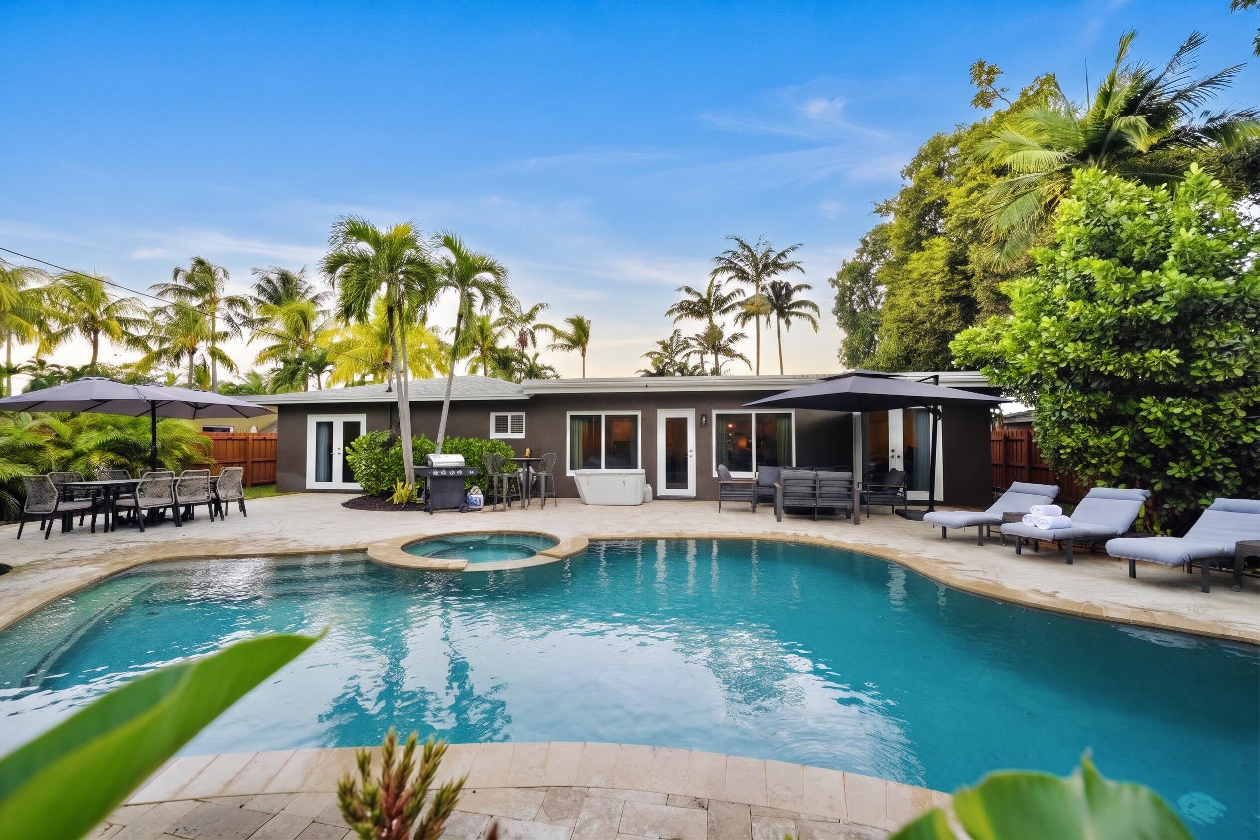 Backyard featuring a paver patio, in-ground swimming pool, integrated spillover spa, and mature palm trees