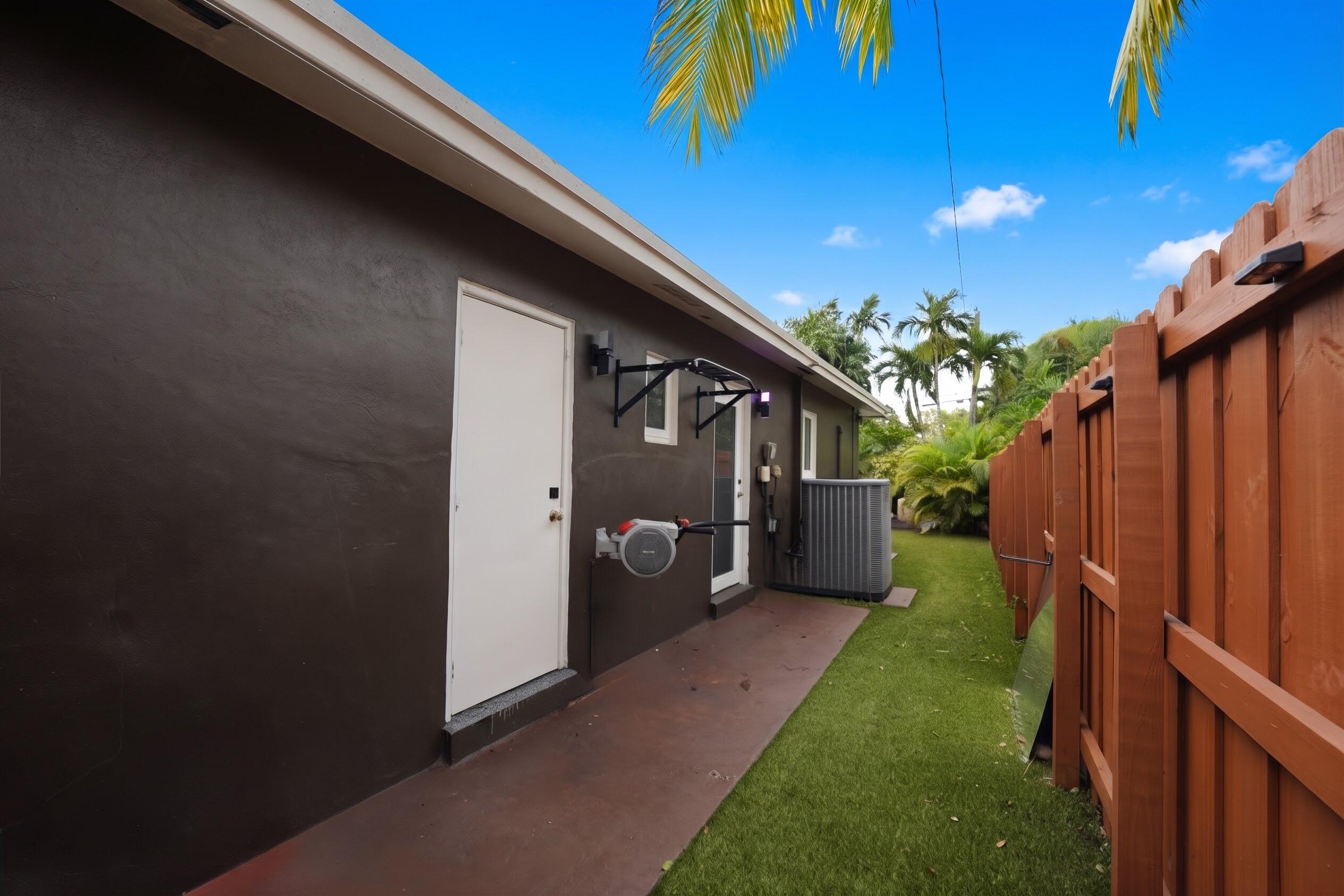 Exterior side yard featuring a concrete patio, synthetic turf lawn, and a solid wood privacy fence