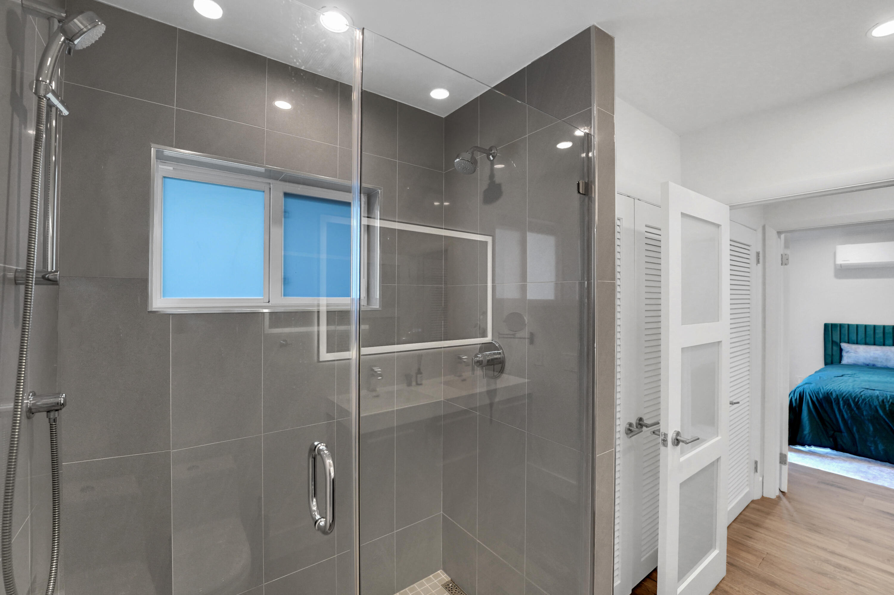 Walk-in shower with floor-to-ceiling gray tile, frameless glass enclosure, and dual shower heads including a handheld wand