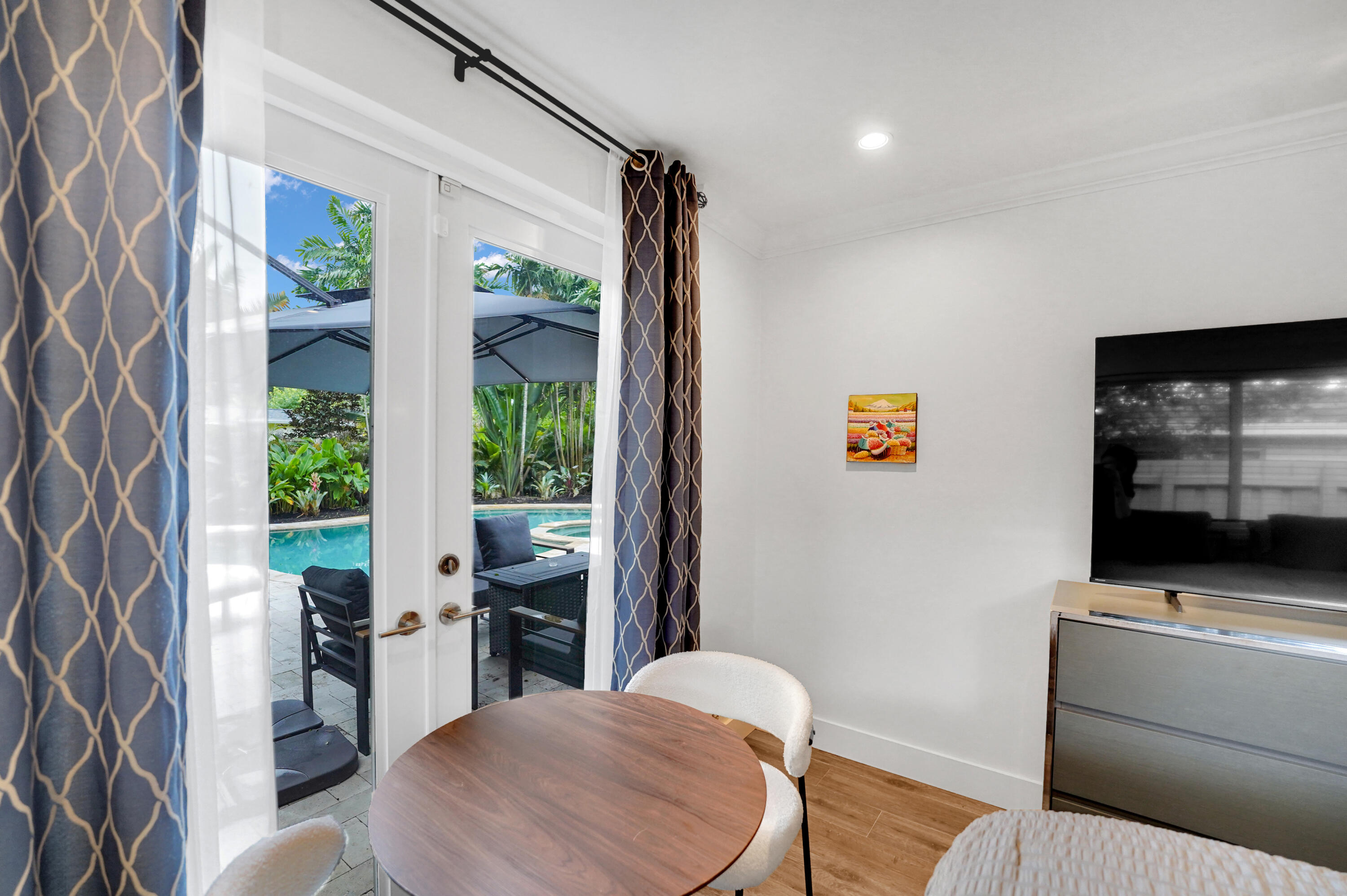Glass-paned French doors opening to a paver patio, swimming pool, and lush landscaping