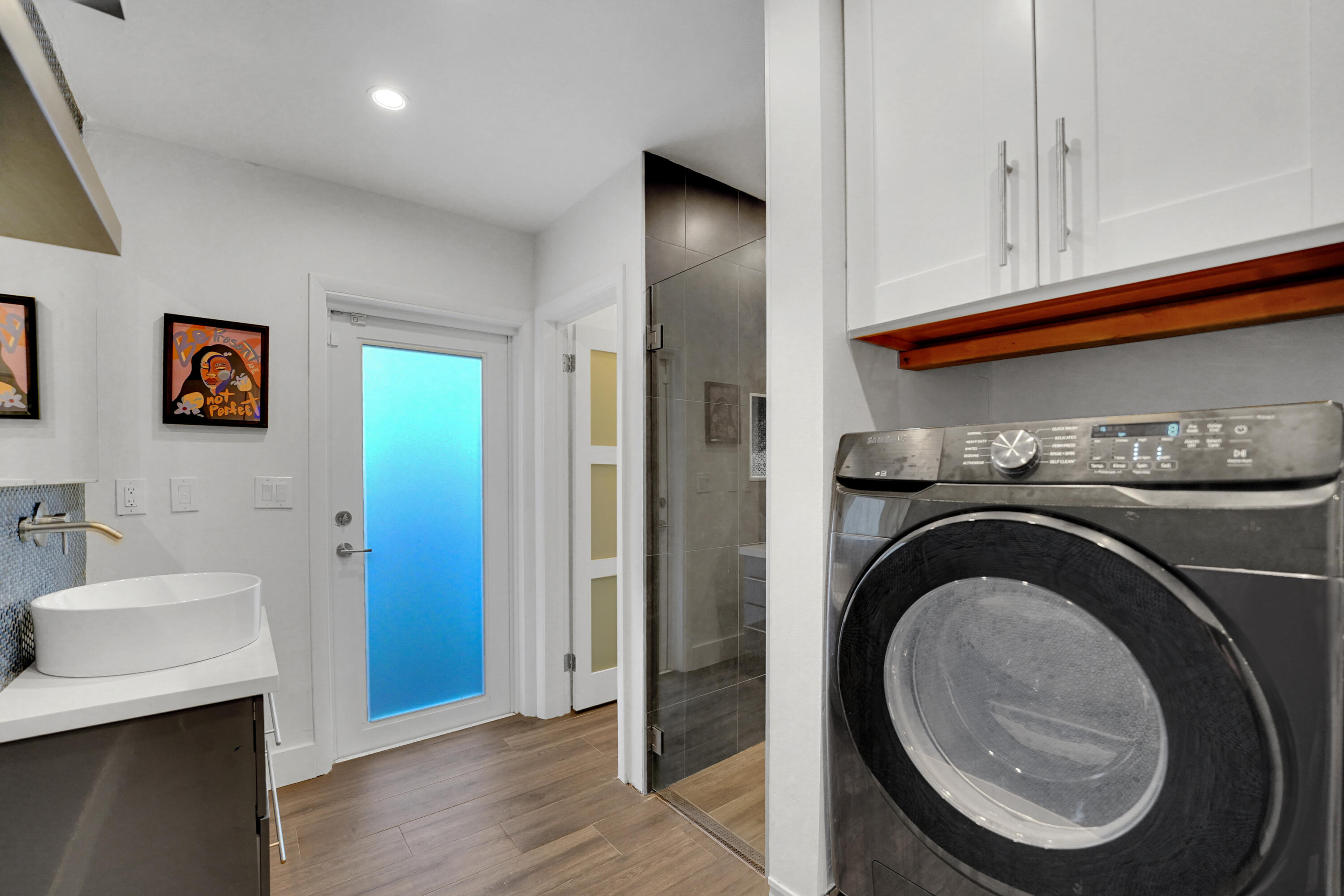Utility space featuring a vessel sink with a wall-mounted faucet, white shaker-style cabinetry, and a frosted glass-panel door
