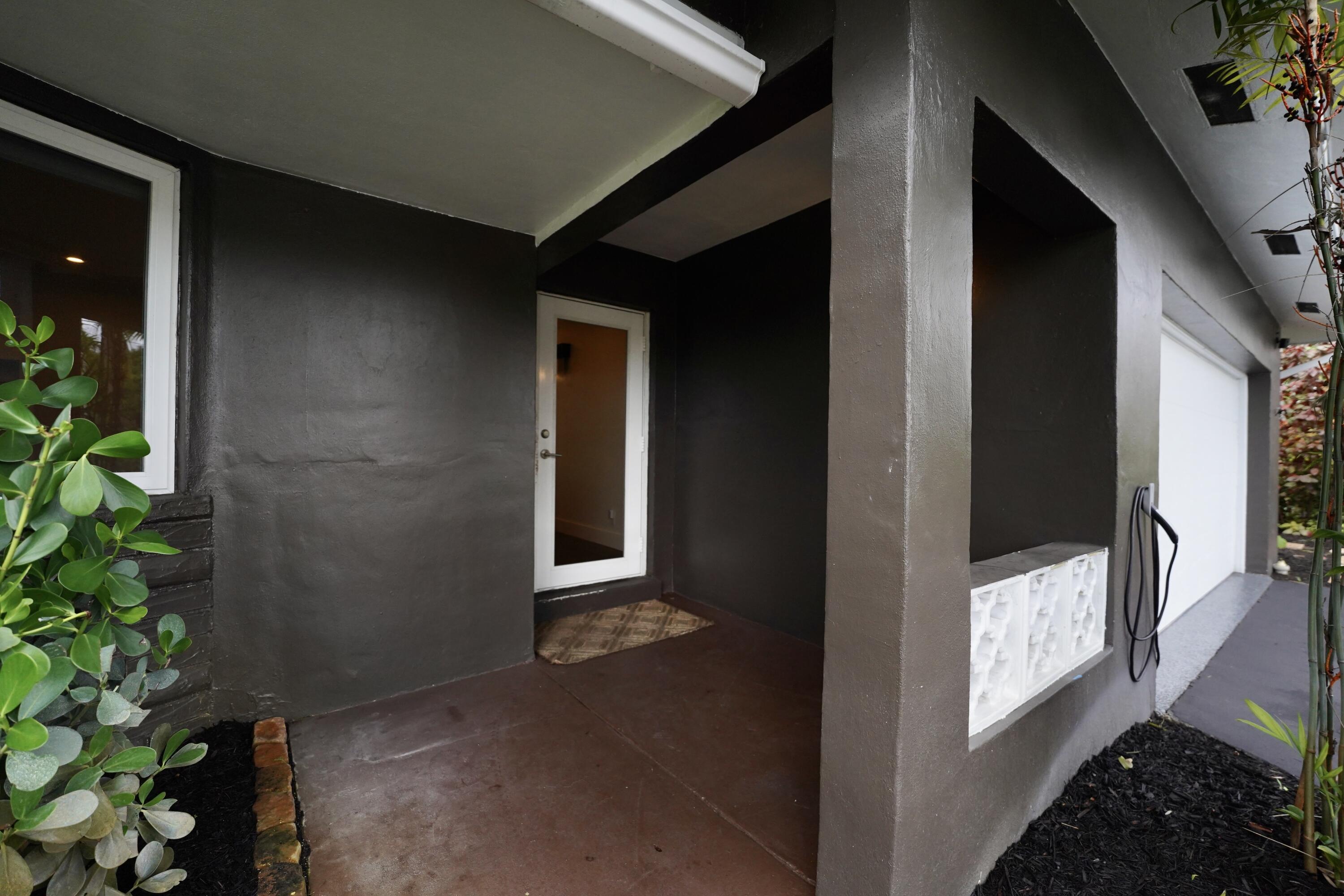 Covered entryway featuring a concrete porch, decorative patterned block screen, white entry door, and attached garage