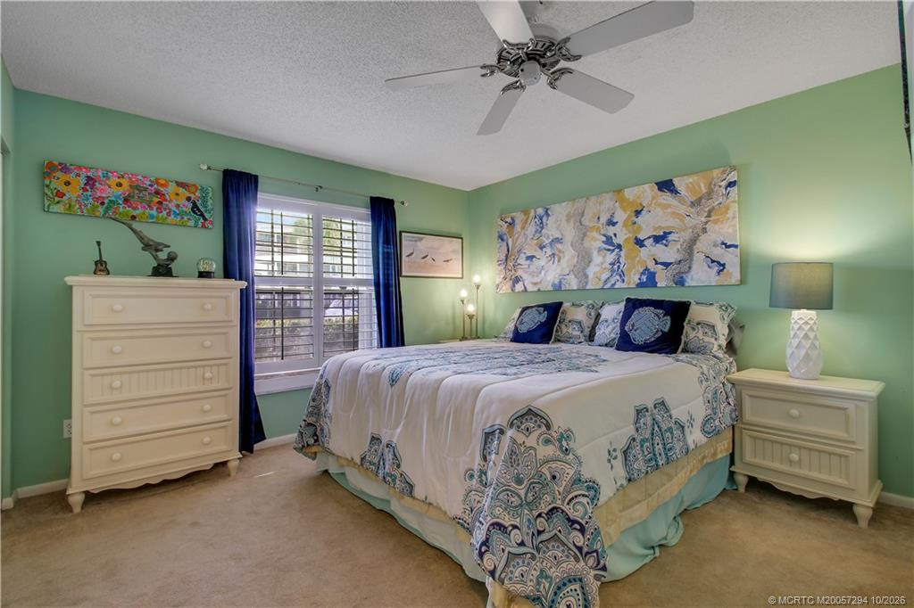 Inviting guest bedroom featuring soothing seafoam-green walls, plush carpeting, ceiling fan, and a large window with plantation shutters. A comfortable retreat with charming coastal appeal.