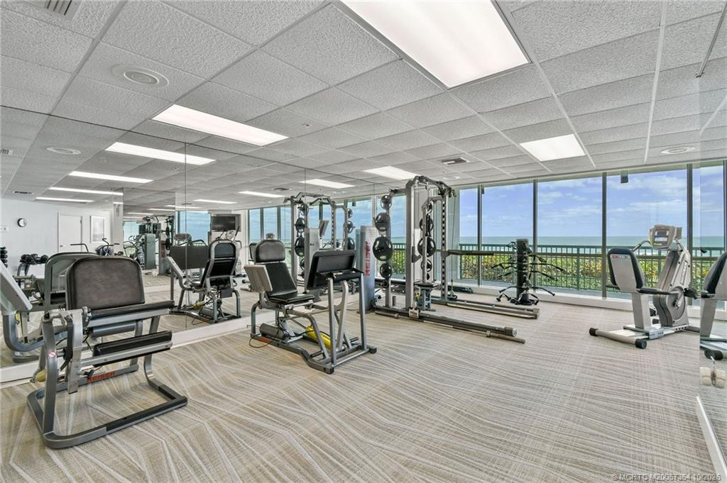 Well-equipped oceanfront fitness center featuring exercise machines, mirrored walls, and expansive windows overlooking the beach.